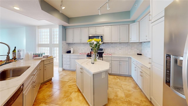 kitchen with tasteful backsplash, light stone countertops, stainless steel appliances, rail lighting, and a sink