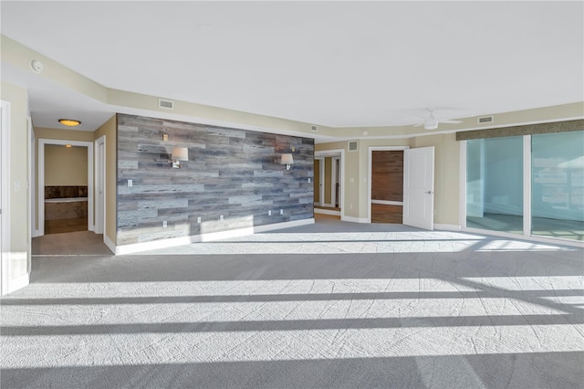 carpeted empty room featuring ceiling fan, visible vents, wood walls, baseboards, and an accent wall
