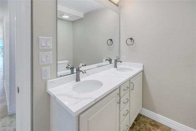 bathroom with baseboards, toilet, double vanity, and a sink