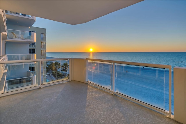 balcony at dusk featuring a water view