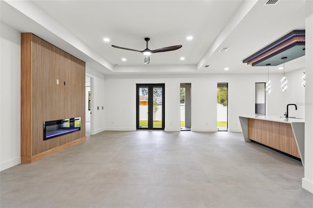 unfurnished living room featuring a large fireplace, a tray ceiling, ceiling fan, and sink