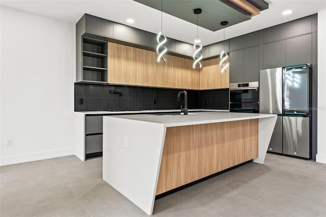 kitchen featuring decorative light fixtures, sink, stainless steel appliances, and an island with sink