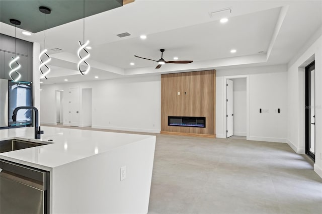 kitchen featuring a center island with sink, decorative light fixtures, ceiling fan, and a tray ceiling