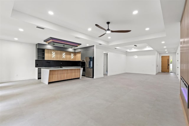 unfurnished living room featuring a tray ceiling and ceiling fan