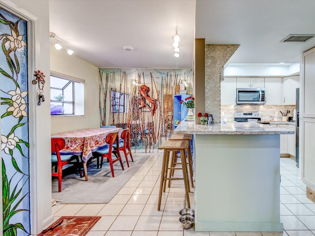 kitchen with appliances with stainless steel finishes, light stone countertops, light tile patterned floors, a kitchen bar, and white cabinetry