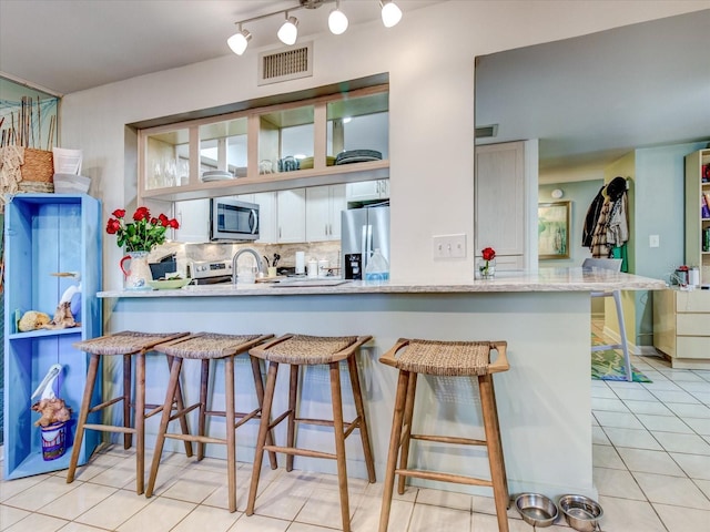 kitchen featuring white cabinets, kitchen peninsula, a breakfast bar area, decorative backsplash, and appliances with stainless steel finishes