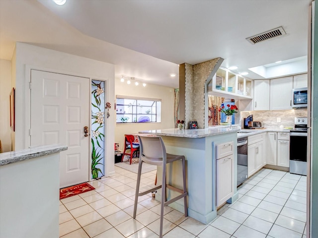 kitchen featuring white cabinetry, light stone counters, a kitchen breakfast bar, tasteful backsplash, and appliances with stainless steel finishes