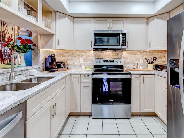 kitchen with light stone counters, stainless steel appliances, light tile patterned floors, white cabinetry, and sink