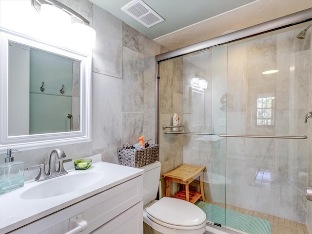 bathroom featuring toilet, vanity, tile walls, and a shower with shower door