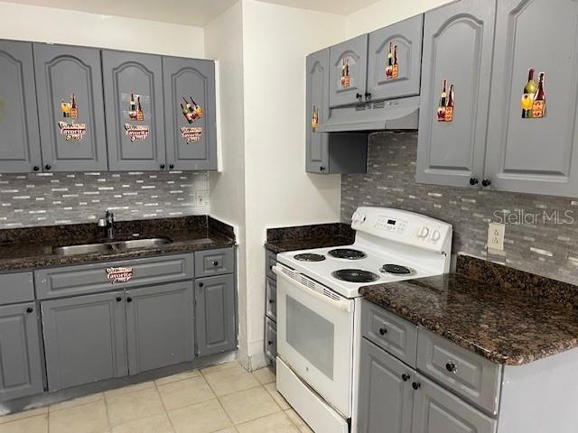 kitchen with dark stone counters, electric stove, sink, gray cabinets, and light tile patterned flooring