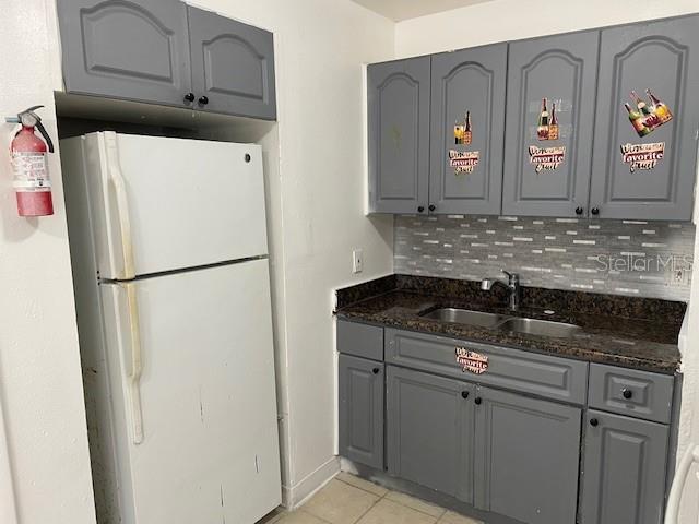 kitchen with sink, white refrigerator, backsplash, dark stone countertops, and light tile patterned flooring