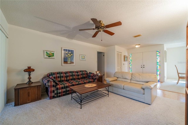 carpeted living room with ceiling fan and a textured ceiling