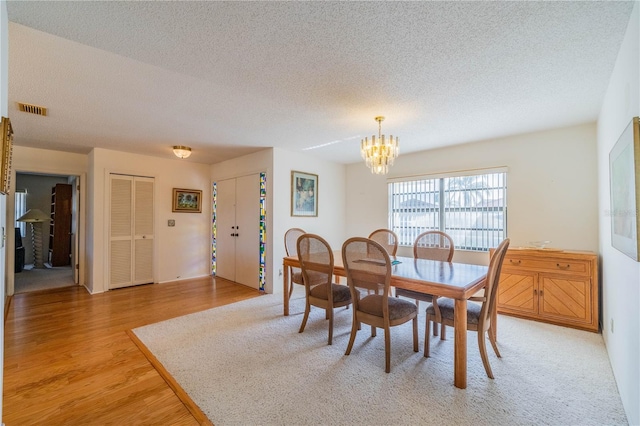 dining room featuring an inviting chandelier, light hardwood / wood-style flooring, and a textured ceiling