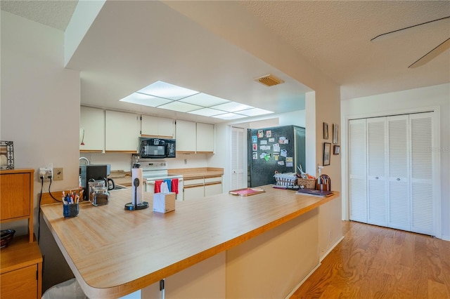 kitchen with black appliances, white cabinets, light hardwood / wood-style floors, kitchen peninsula, and a textured ceiling