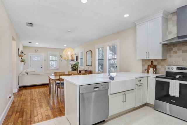 kitchen featuring white cabinetry, appliances with stainless steel finishes, kitchen peninsula, and wall chimney range hood