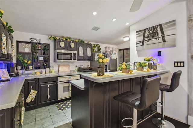 kitchen with backsplash, light tile patterned floors, a kitchen bar, kitchen peninsula, and stainless steel appliances