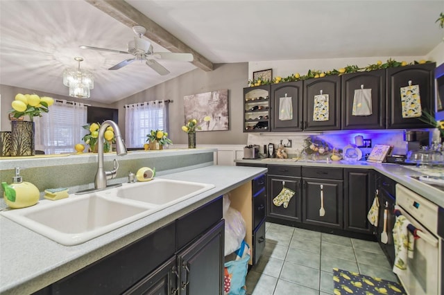 kitchen with sink, lofted ceiling with beams, oven, light tile patterned floors, and ceiling fan with notable chandelier