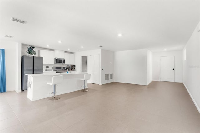 kitchen with a kitchen island with sink, white cabinets, sink, appliances with stainless steel finishes, and a kitchen bar