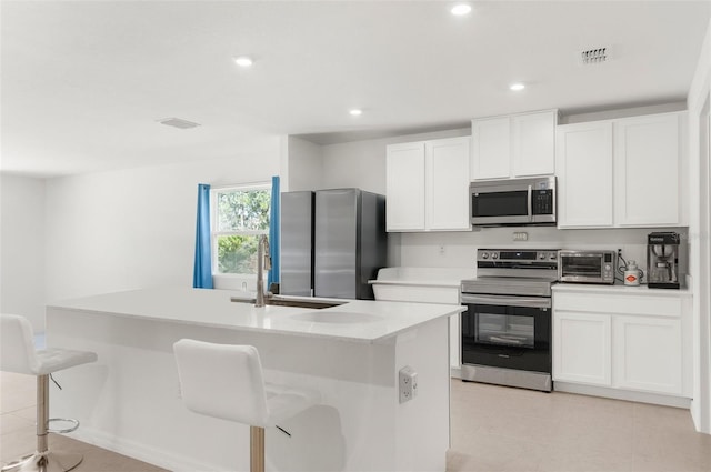 kitchen featuring white cabinetry, a kitchen island with sink, a breakfast bar, and appliances with stainless steel finishes