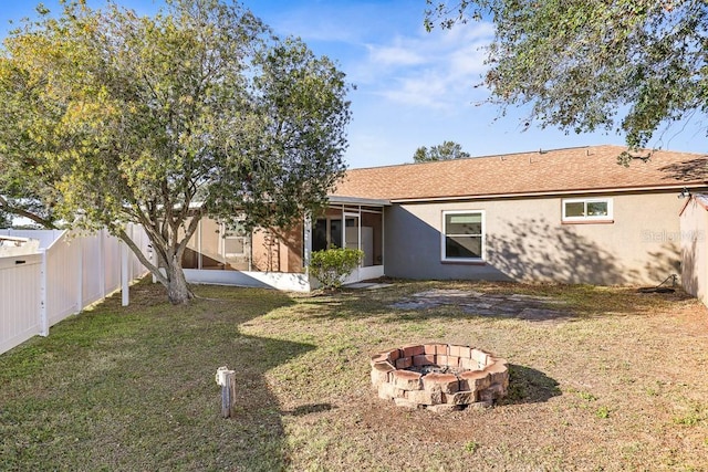 rear view of house featuring a sunroom, a yard, and an outdoor fire pit