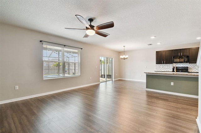 unfurnished living room featuring ceiling fan with notable chandelier, a textured ceiling, and dark hardwood / wood-style flooring