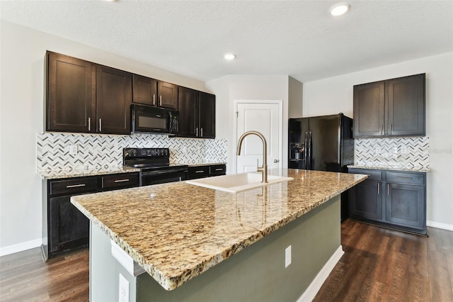 kitchen featuring backsplash, light stone counters, a kitchen island with sink, sink, and black appliances