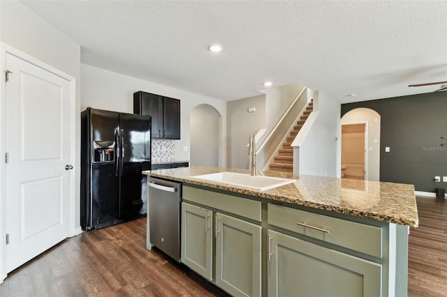 kitchen with light stone countertops, sink, black refrigerator with ice dispenser, stainless steel dishwasher, and a kitchen island with sink