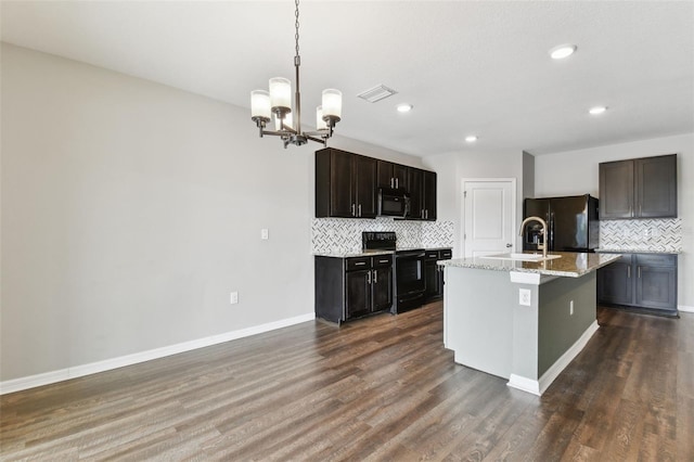 kitchen with backsplash, black fridge, electric range, and a center island with sink