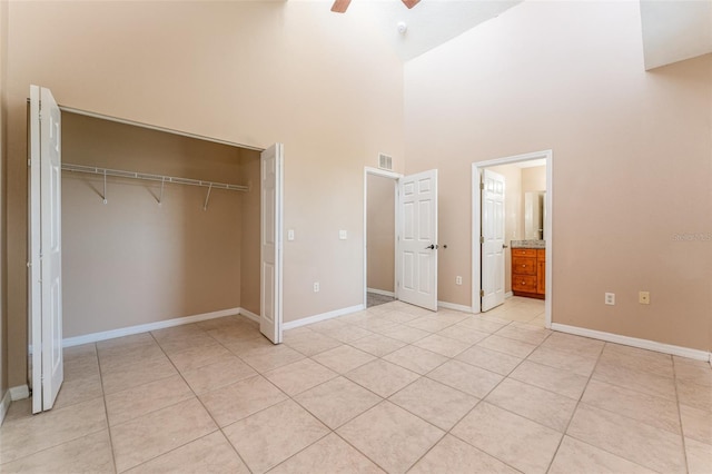 unfurnished bedroom with a high ceiling, a closet, connected bathroom, ceiling fan, and light tile patterned flooring