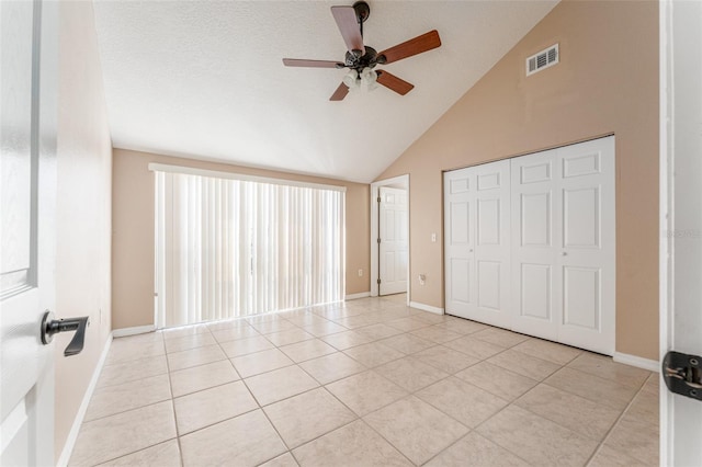 unfurnished bedroom featuring a closet, a textured ceiling, ceiling fan, light tile patterned flooring, and vaulted ceiling