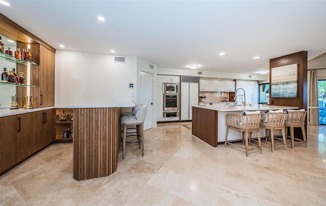 kitchen with a kitchen island with sink, built in appliances, backsplash, and a breakfast bar area