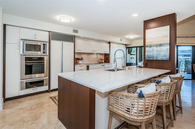 kitchen with white cabinetry, built in appliances, sink, and a center island with sink