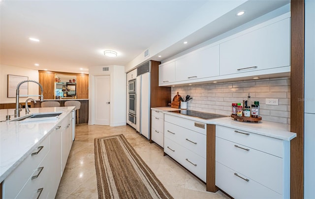 kitchen featuring sink, white cabinets, decorative backsplash, stainless steel appliances, and light stone countertops