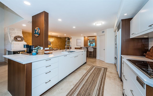 kitchen featuring cooktop, sink, a center island with sink, and white cabinets