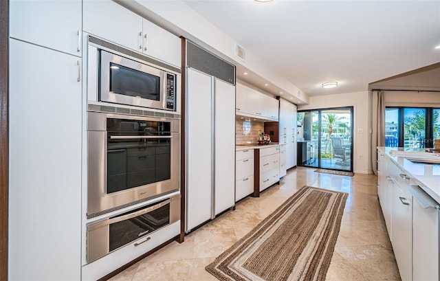 kitchen with tasteful backsplash, white cabinetry, and built in appliances