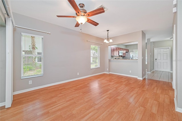 unfurnished living room with ceiling fan with notable chandelier and light hardwood / wood-style flooring