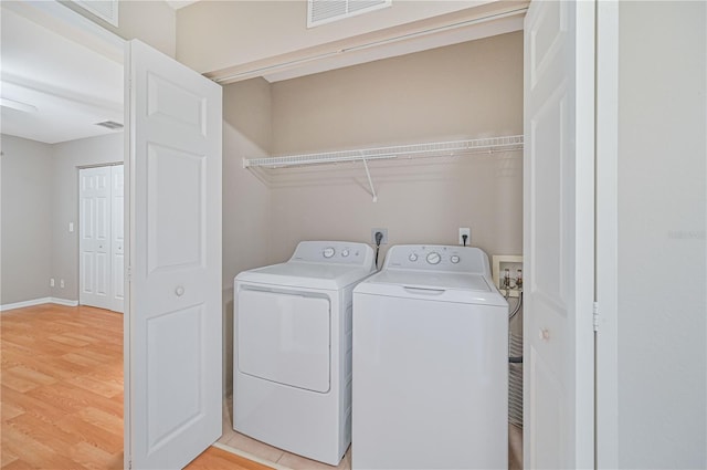 laundry room with washing machine and clothes dryer and light hardwood / wood-style floors