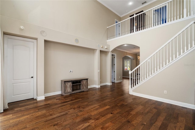 unfurnished living room with a towering ceiling, dark wood-type flooring, and ornamental molding