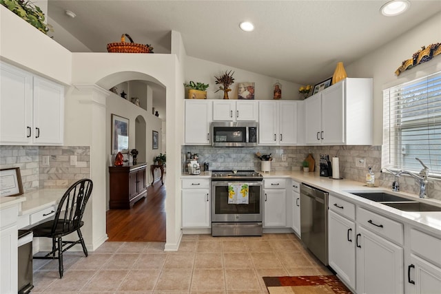 kitchen with light tile patterned flooring, appliances with stainless steel finishes, white cabinetry, lofted ceiling, and sink