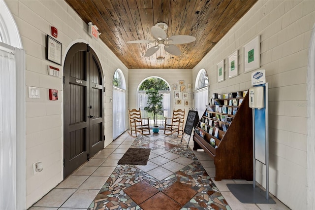 interior space featuring brick wall, light tile patterned flooring, ceiling fan, and wood ceiling