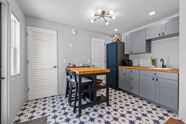 kitchen featuring gray cabinetry, butcher block counters, sink, and a chandelier