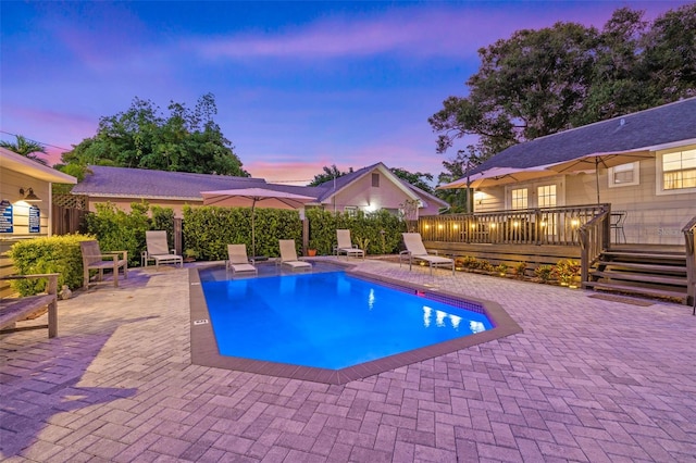 pool at dusk featuring a patio and a wooden deck