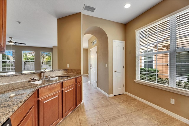 kitchen with light stone countertops, light tile patterned flooring, ceiling fan, and sink