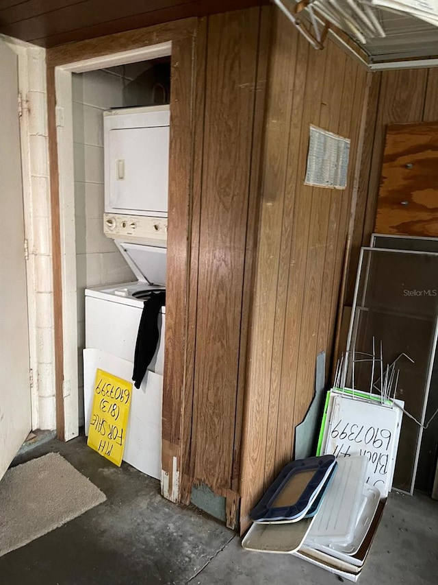 washroom featuring wood walls and stacked washing maching and dryer