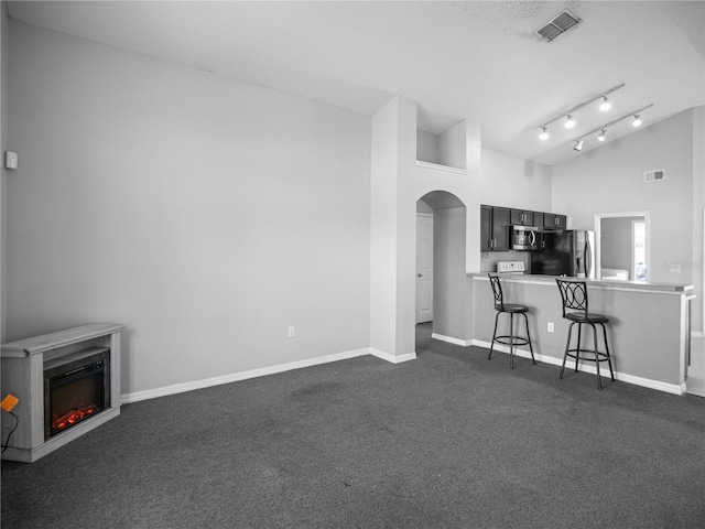 unfurnished living room featuring a towering ceiling and dark carpet