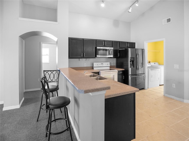 kitchen with stainless steel appliances, a kitchen breakfast bar, kitchen peninsula, a towering ceiling, and washer and clothes dryer