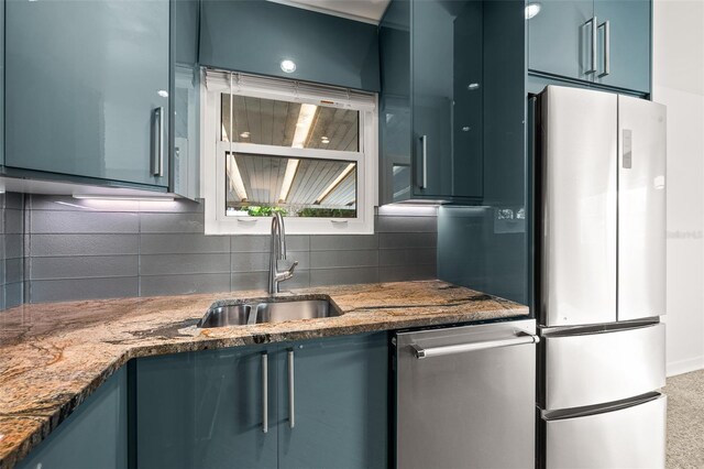 kitchen with blue cabinets, a sink, dark stone countertops, freestanding refrigerator, and decorative backsplash