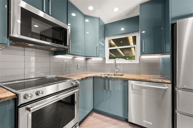 kitchen featuring light stone counters, tasteful backsplash, appliances with stainless steel finishes, and a sink