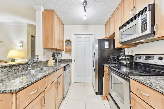 kitchen with appliances with stainless steel finishes, light brown cabinetry, track lighting, dark stone counters, and sink