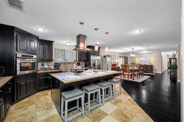 kitchen with stainless steel appliances, a kitchen bar, backsplash, visible vents, and a kitchen island
